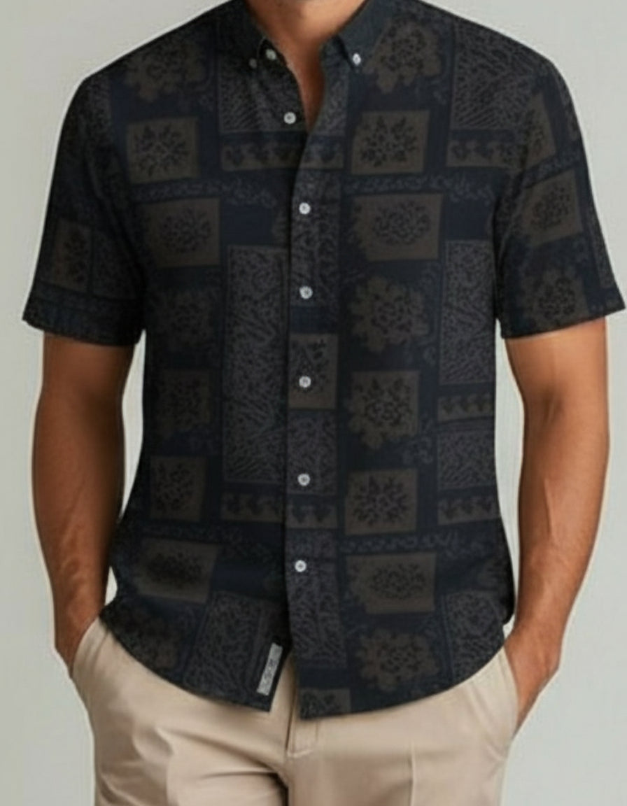 Man wearing a dark patterned shirt with beige pants on a plain background